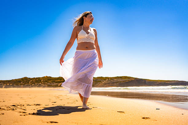 The woman is holding her shoes in her hand. She feels free. She walks barefoot on the beach.