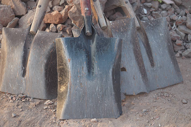 Different shovels rest on the ground near a pile of gravel and rocks.