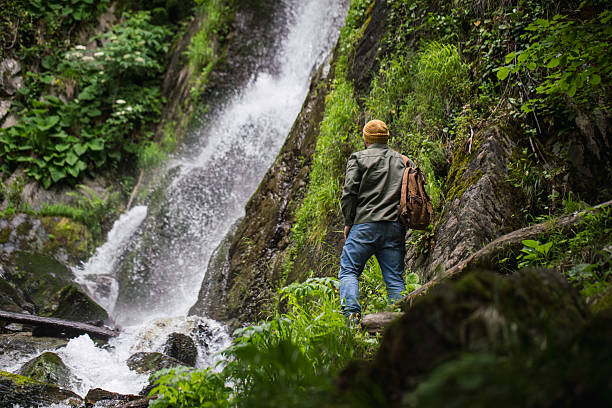 istock Backpacker Enjoying a Scenic Waterfall in a Forested Mountain Landscape 2220274148
