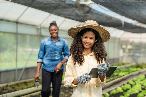 Next Generation Farmer Using a Tablet for Smart Farming, with Her Proud Mother in the Background.