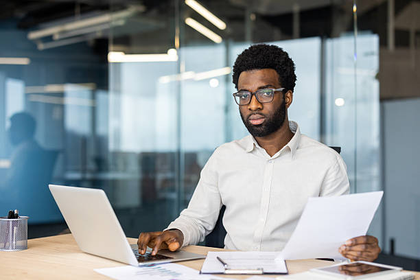 istock A focused professional works on his laptop while reviewing important documents in a modern office. 2220277530