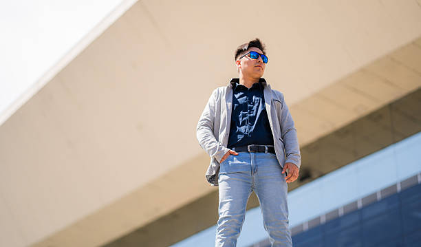 Young man in sunglasses and smart casual attire posing confidently in front of a modern building. Perfect image to represent leadership, confidence, success and contemporary corporate lifestyle.