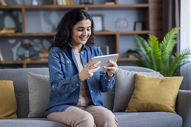 istock A cheerful young woman is engrossed in her tablet while relaxing on a comfy sofa at home. 2220283395