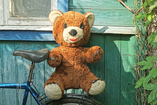 one big brown toy bear sits on a bicycle rack near a green wall on a summer street