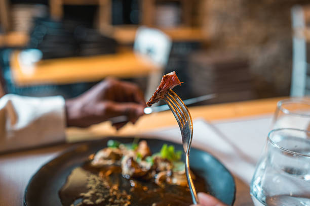 A close-up of a fork holding a bite of gourmet food, presented in a fine dining restaurant. Warm lighting highlights elegant plating and refined atmosphere.
