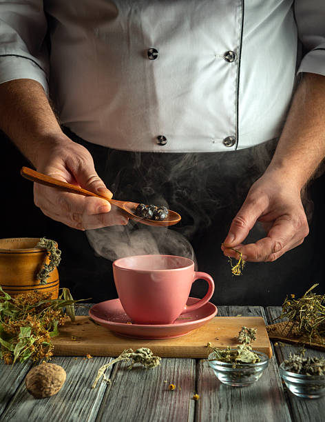 istock A chef carefully prepares herbal tea, adding dried herbs to a pink cup. The warm steam rises, creating a cozy atmosphere in a rustic kitchen. The surrounding ingredients add to the artisanal vibe 2220298745