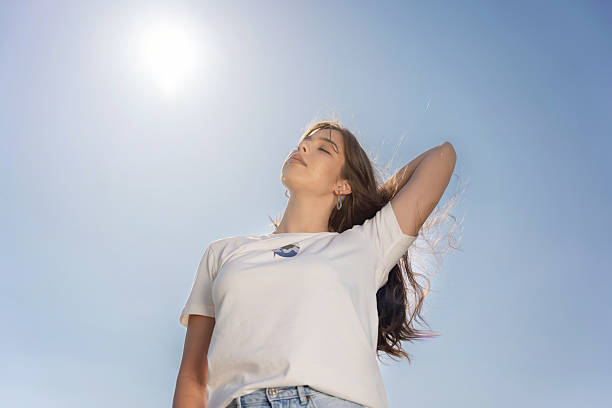 istock Young Woman Enjoying Sunlight with Relaxed Pose Against Clear Blue Sky 2220300990