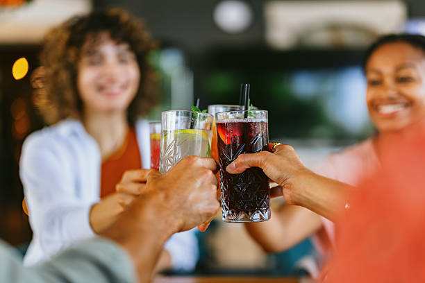 A joyful group of friends raises non-alcoholic drinks in a restaurant setting. The image captures a moment of laughter and togetherness, highlighting friendship and enjoyment in a casual dining environment.