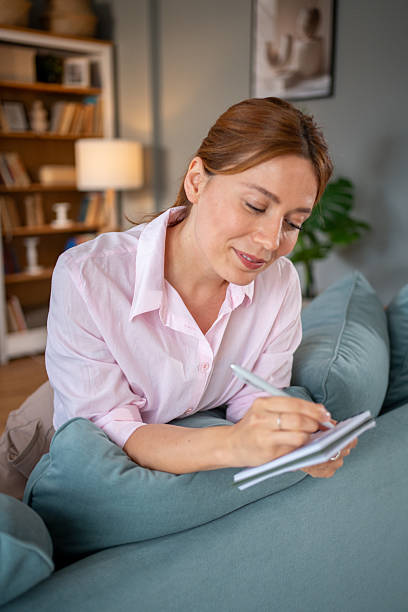 istock Woman lying on sofa and writing in notebook at home 2220303705