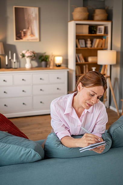 istock Woman lying on sofa writing in notebook in cozy living room 2220303714
