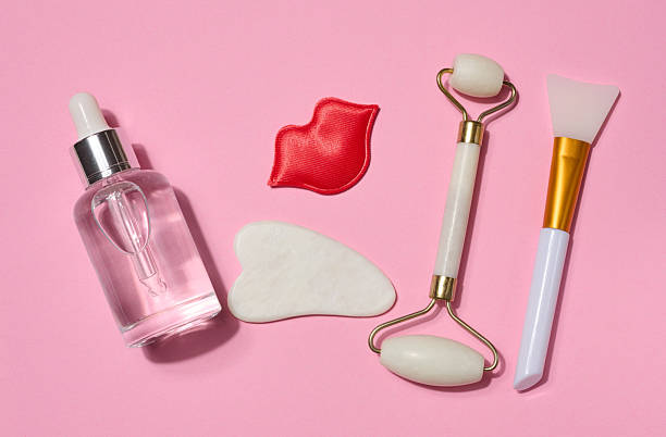 istock Bottle with transparent serum, red decorative lips, white gua sha scraper and facial massage roller placed on pink background. 2220308047