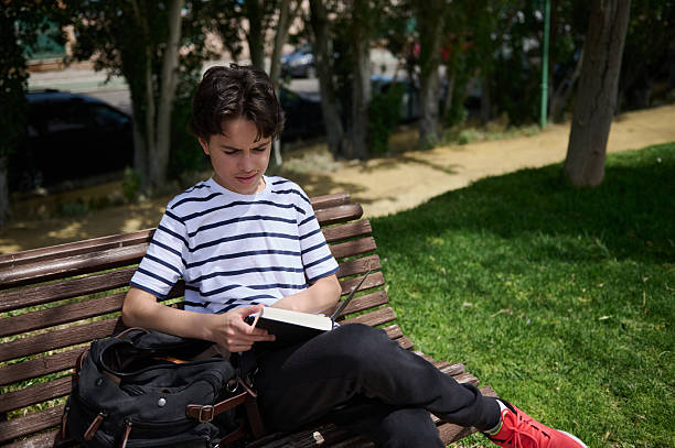 istock Young Man Reading a Book on a Park Bench During a Sunny Day 2220309289