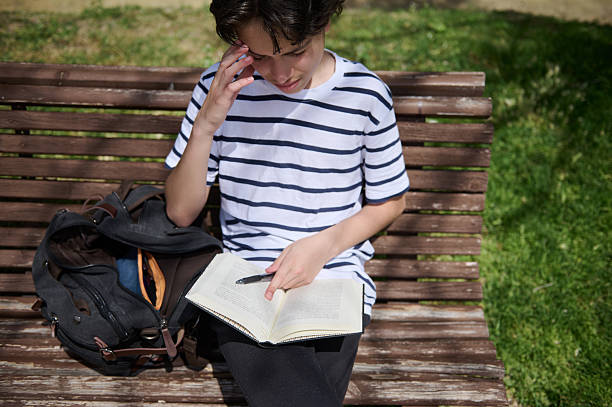 istock Young Individual Reading a Book Outdoors on a Wooden Bench During a Sunny Day 2220309295
