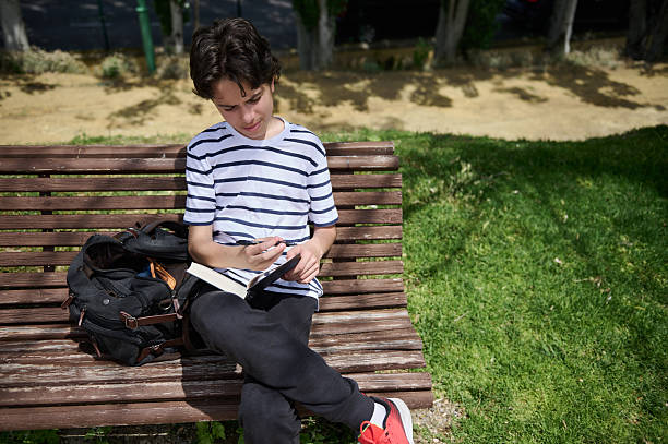 istock Young Boy Writing in a Notebook on a Park Bench in Nature 2220309336