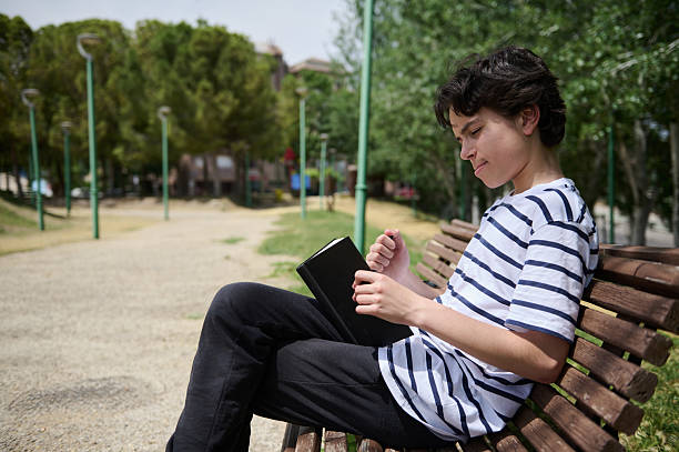 istock Teenager Relaxing on a Park Bench While Reading a Book on a Sunny Day 2220309341