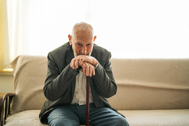 istock Lonely Elderly Man Sitting Thoughtfully at Home with Walking Cane 2220311526