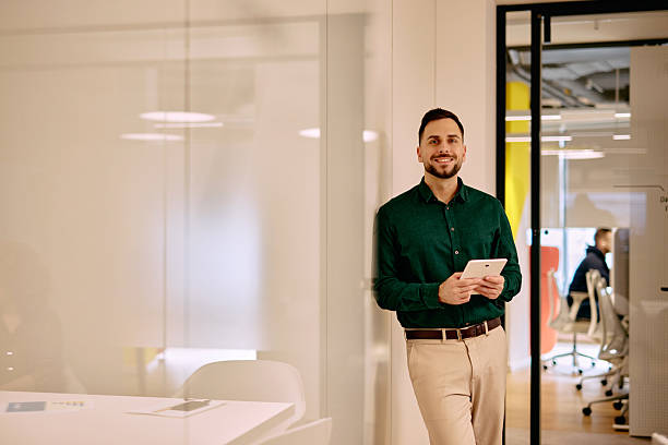 istock Young businessman holding tablet and smiling in modern office 2220311660