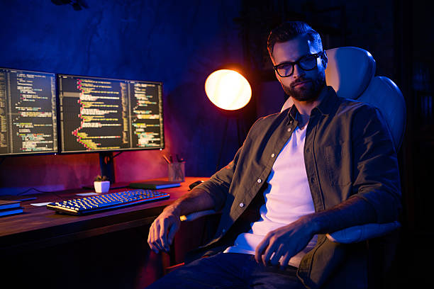 istock Photo of serious smart guy sit look camera lamp light operating server protection dark loft space business center 2220314808