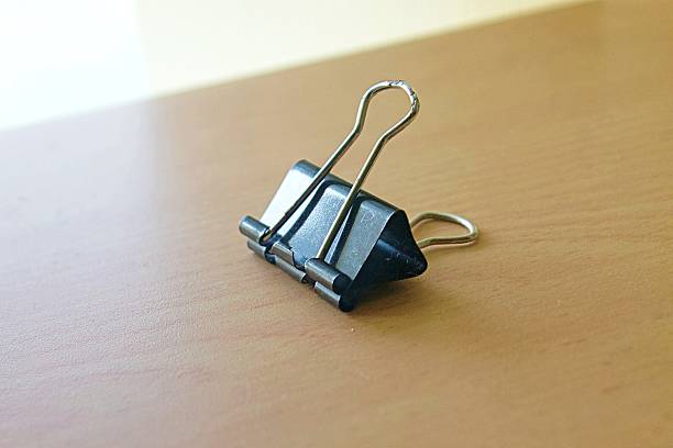 Side Angle Shot of Black Binder Clip on Wooden Desk with Soft Light