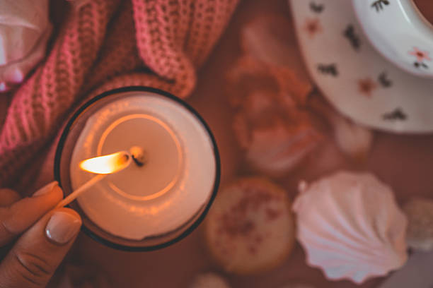 Flat lay with a cozy pink tea setting, meringues, candle being lit, tulips, and soft textures. Feminine and romantic atmosphere with sweet treats and warm ambiance