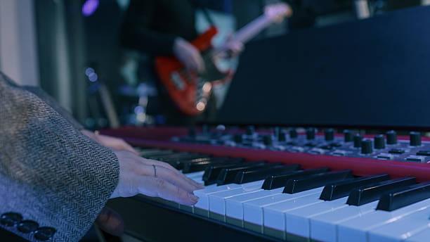 istock Close-up of hands playing electronic keyboard during live music performance with blurred bassist in background under blue lighting 2220332797