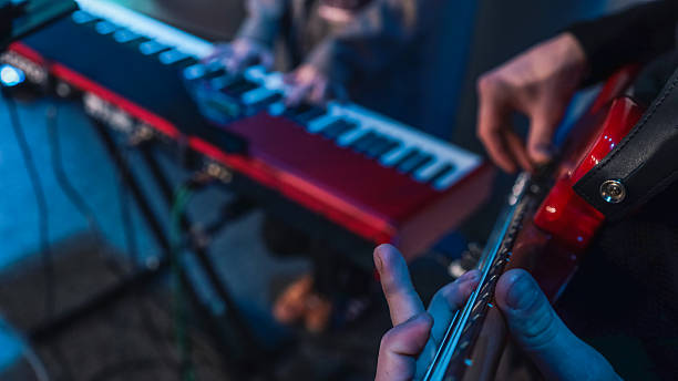 istock Close-up of hands playing electronic keyboard during live music performance with blurred bassist in background under blue lighting 2220332805