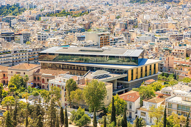 A city view with a large building in the middle. The building is surrounded by trees and has a lot of windows. August 9, 2024 Athens Greece
