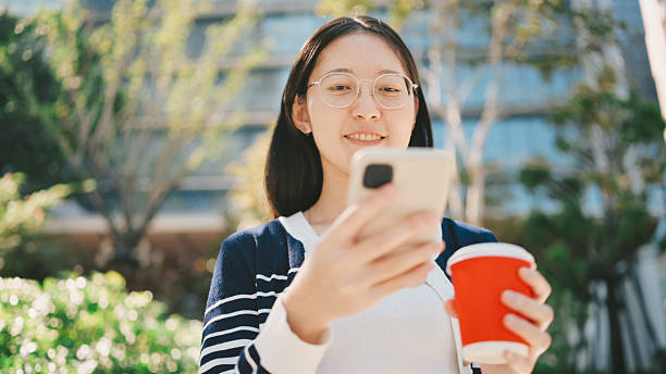 istock happy asian gen z woman holding coffee and using smartphone outdoors checking mobile notifications and enjoying coffee break outside in city environment 2220342968