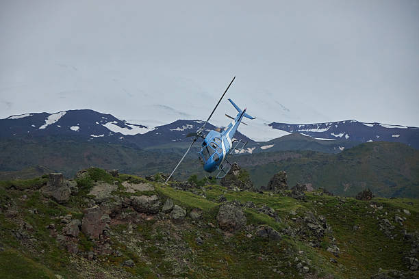 istock helicopter navigates a challenging flight path low above rocky landscapes in Iceland, surrounded by lush greenery and distant snow-capped peaks under an overcast sky 2220350555