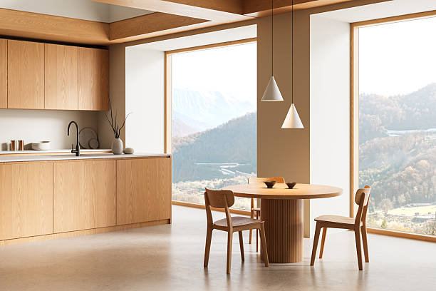 Modern minimalist wooden kitchen interior with round dining table and pendant lights, featuring mountain landscape through large windows. 3D Rendering