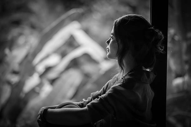 Lovely young woman wearing an old dress, standing against an old windows.