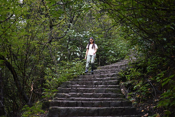 A girl walks down stone steps surrounded by thick green forest during a nature hike. Shot on the hiking trail to Korigad fort in Lonavala near Pune, Maharashtra during Monsoon season.