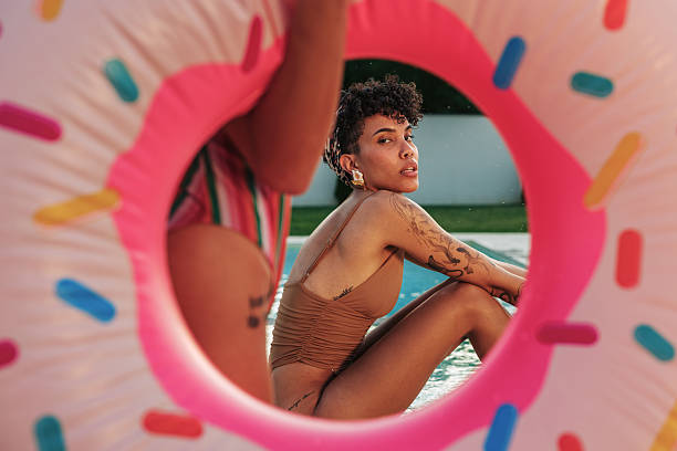 Two young women are having fun at the poolside of their holiday home during summer vacation, with an inflatable donut ring