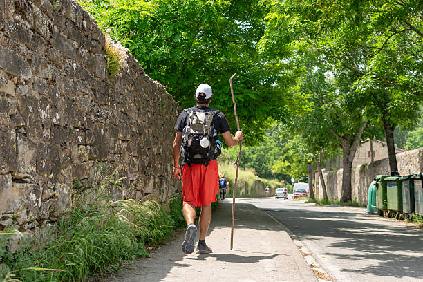 Senior couple walking, carrying their backpacks with scallops hanging, symbol of the pilgrimage, walking the camino de Santiago, ancient pilgrimage route .Directional milestone in the background.