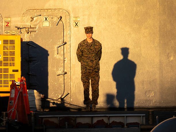 A lieutenant of the United States Marine Corps stands on the deck of USS America, LHA-6, an amphibious assault ship of the United States Navy docked at Garden Island naval base in Sydney Harbour. This image was taken from the opposite side of Woolloomooloo Bay on a cold and sunny afternoon approaching sunset on 16 June 2025.