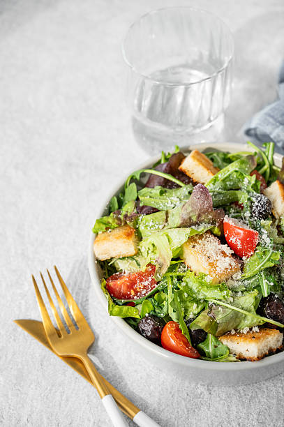 Salad with lettuce, tomatoes, croutons, olives and parmesan cheese in a bowl on a light background