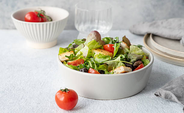 Vegetarian salad with lettuce, tomatoes, croutons and olives in a bowl on a light background
