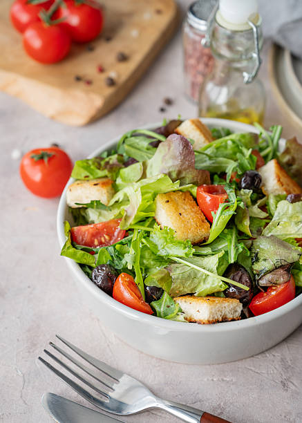 Vegetable salad with lettuce, tomatoes, croutons and olives in a bowl on a light background