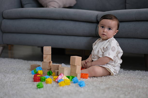 A cute little girl enjoys playing with large colorful dice, especially dropping them. She pretends to be sorry at first, but then smiles smugly.