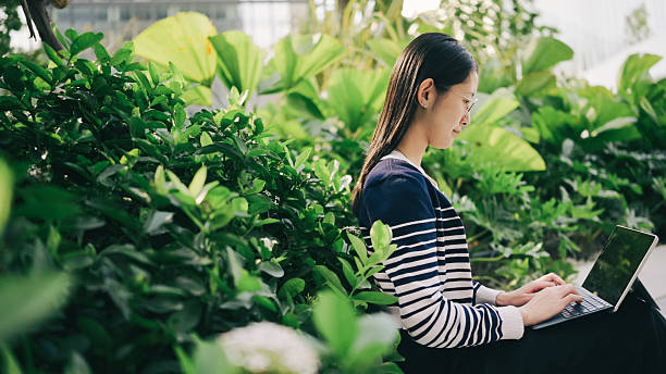 A Gen Z woman focuses on a tablet while sitting in the park, symbolizing flexibility in learning and working.  remote work, online class, digital workspace, tablet use, tech-savvy student, greenery, education tech.