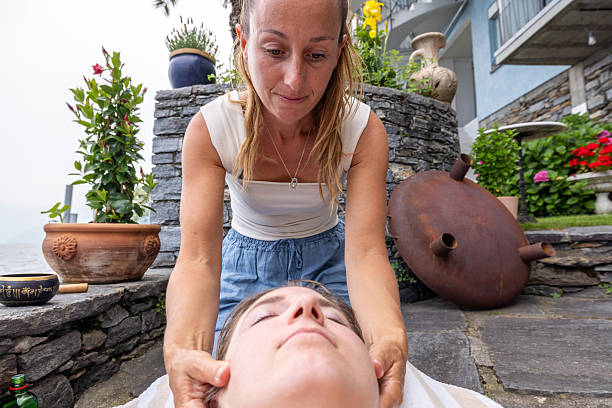 Woman enjoying a therapeutic facial massage outdoors. Close-up of hands applying gentle pressure in serene garden. Wellness and relaxation in natural setting.