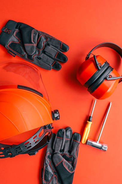 istock Safety equipment including protective gloves, earmuffs, face shield and hand tools on vibrant orange background, industrial work concept 2220382980