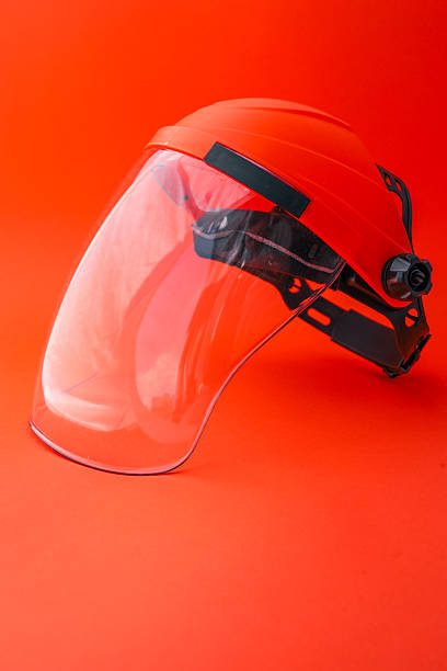 istock Protective face shield with transparent visor and orange headgear, isolated on bright red background, used for safety during industrial, construction or gardening work 2220382982