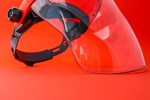 istock Protective face shield with transparent visor and orange headgear, isolated on bright red background, used for safety during industrial, construction or gardening work 2220382991