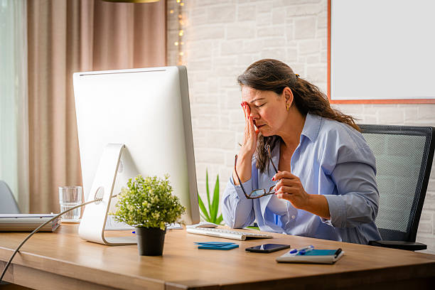 istock Tired woman touching her eyes while working on computer. Eye fatigue at the office, working late pull glasses off sitting at the desk online working 2220383262