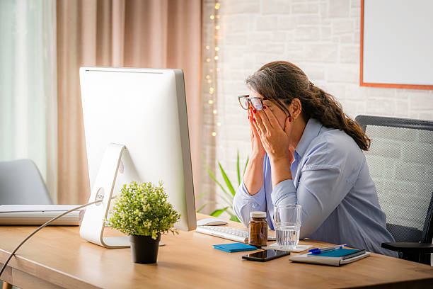 Woman working on computer tired and overworked rubbing her eyes, working late at home or office sitting at the desk, pills, mobile phone and documents