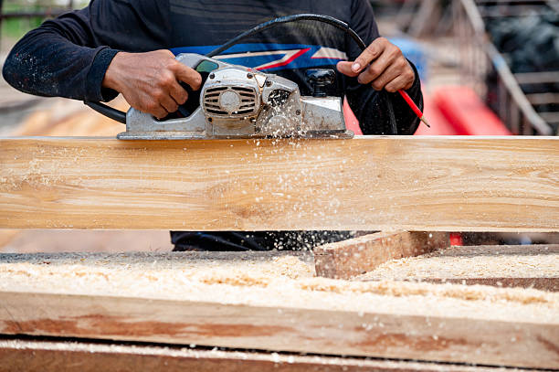 istock Male carpenter hand using an electric planer on wooden plank in workshop 2220383352