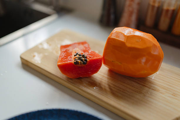 Freshly cut papaya fruit displaying vibrant orange flesh and black seeds on a wooden cutting board