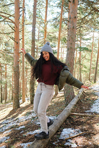 Young woman carefully balancing on a log while enjoying a leisurely walk through a serene snowy forest