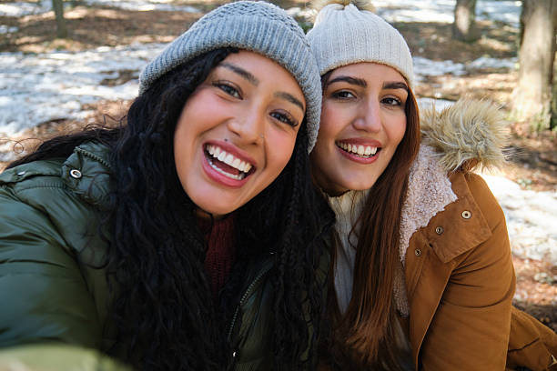 Group of millenial young female adult friends enjoying wintertime and in a snow filled park